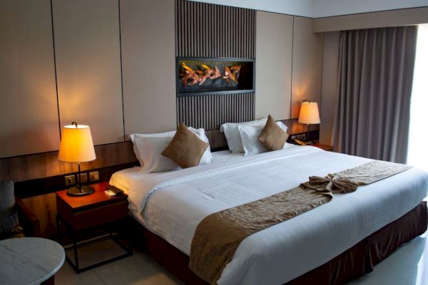 A cozy hotel room features a large bed with white linens and brown accents, bedside tables with lamps, and a modern design.