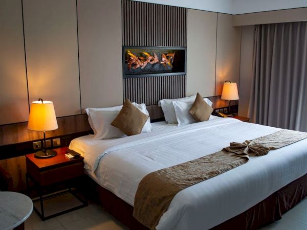 A cozy hotel room features a large bed with white linens and brown accents, bedside tables with lamps, and a modern design.