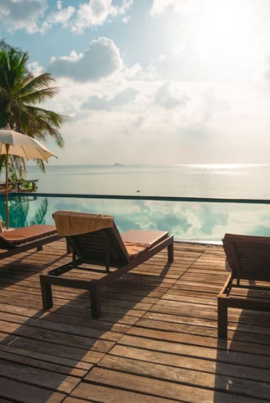 A tranquil poolside scene with lounge chairs, umbrellas, and a calm ocean backdrop under a partly cloudy sky, suggesting a relaxing vacation.