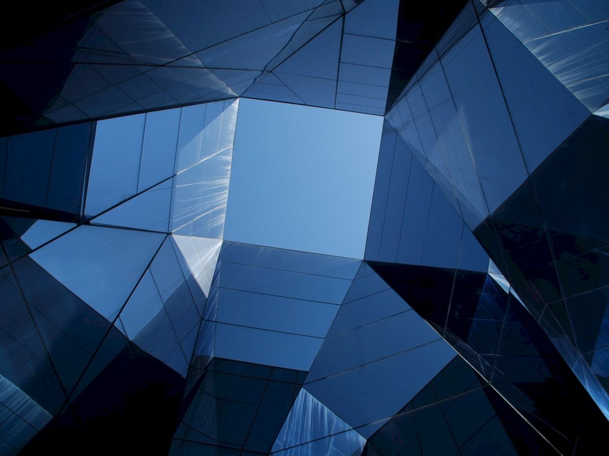 This image shows a view of the sky framed by angular, reflective glass buildings arranged in a geometric pattern, creating a modern architectural feel.
