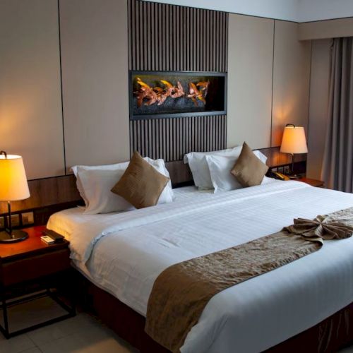 A well-lit hotel room with a large bed, two bedside tables with lamps, a modern fireplace, and curtains covering a window, creating a cozy ambiance.