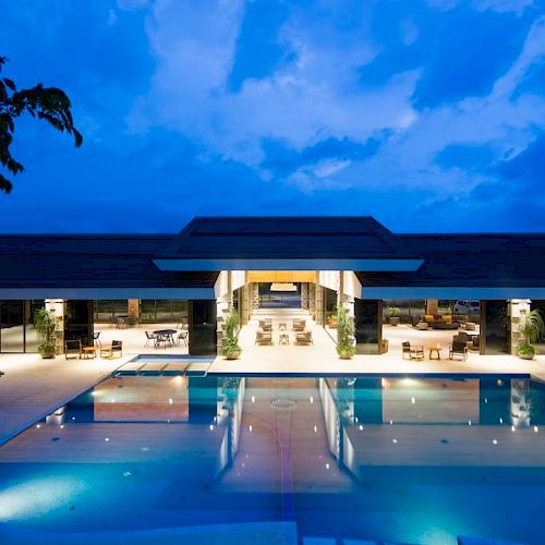 A luxurious building with large windows and an outdoor pool under a twilight sky.
