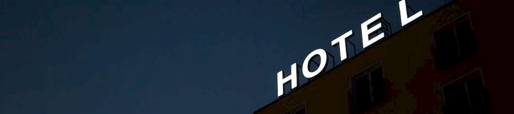 The image shows a building with the word "HOTEL" in illuminated letters at the top, set against a dark sky, with the letter 'L' partially lit.