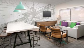 A modern room features a white marble table with bar stools, a sofa with colorful pillows, a wall-mounted TV, and contemporary decor.