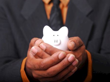 A person in a suit is holding a small white piggy bank with both hands, emphasizing the importance of saving and financial security.