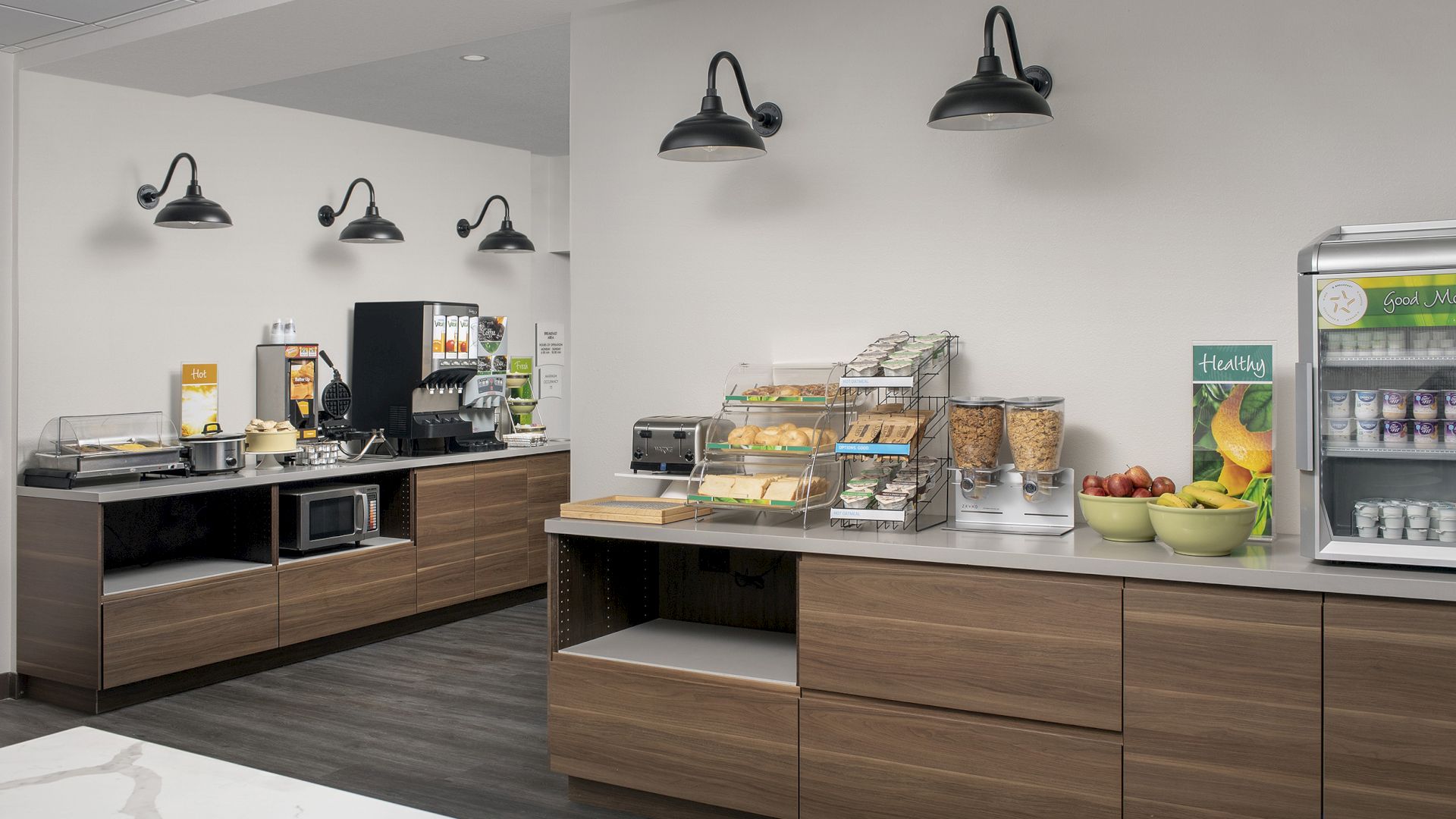 The image shows a modern breakfast station with various appliances, cereals, fruits, and a refrigerator stocked with yogurt and beverages.