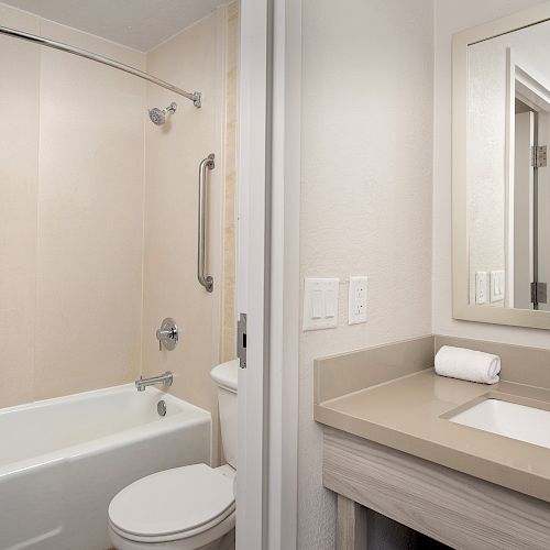 This image shows a clean bathroom with a white bathtub, a shower curtain, a toilet, a sink with a countertop, and a mirror above it.