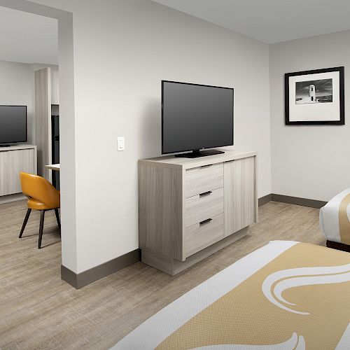 The image shows a hotel room with two beds, two TVs on dressers, a desk with an orange chair in one corner, and a framed picture on the wall.