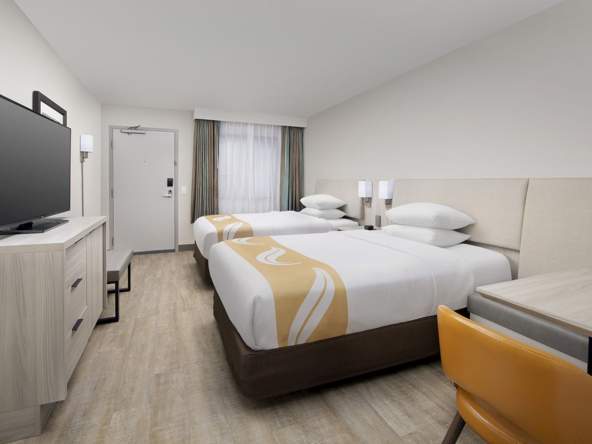 A modern hotel room with two neatly made beds, a wall-mounted TV, wooden furniture, and a desk with a yellow chair, featuring a clean and minimalist design.