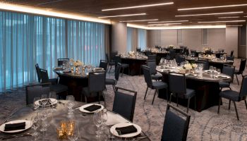 This image shows a banquet hall with round tables set for a formal event, featuring floral centerpieces, glassware, and black napkins, under warm lighting.
