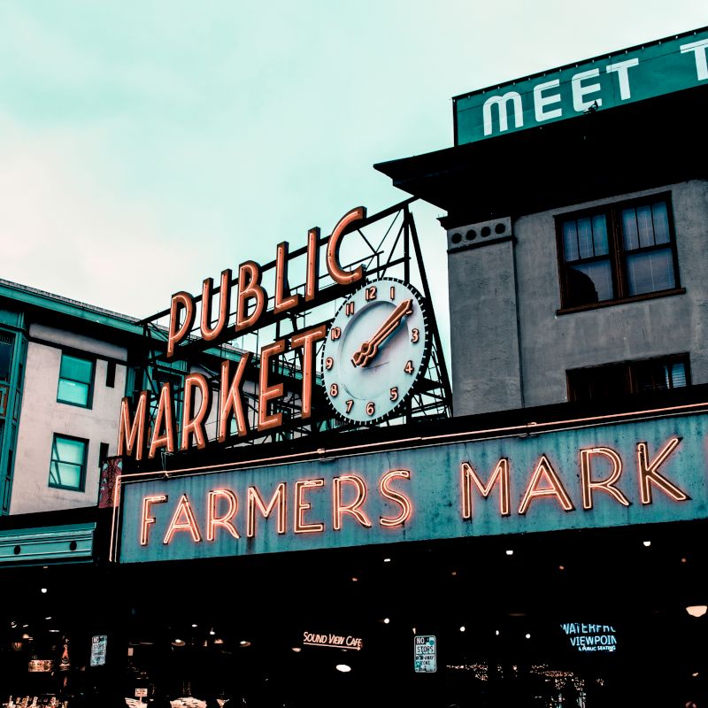 This image shows a neon sign for "Public Market" and "Farmers Market" on a building, presumably at a marketplace, with a visible clock.