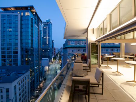 A modern balcony overlooking a city skyline at dusk, with chic furniture and tables, creating a sleek and inviting outdoor space.