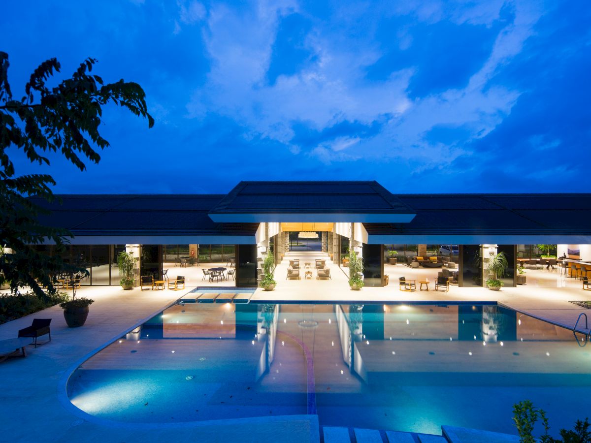 A luxurious building with an illuminated swimming pool and lounge area at dusk, surrounded by elegant seating and modern architecture.