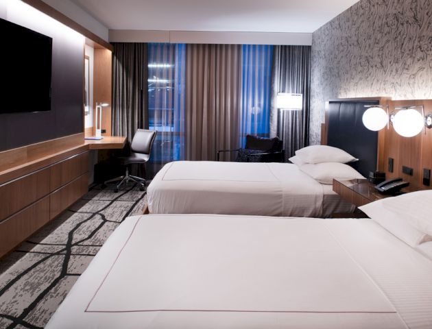A modern hotel room with two beds, desk, lamp, TV, and patterned wall design. The atmosphere is neat and stylish.