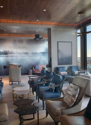 A modern lounge area with plush seating, a wall mural of a cityscape, large windows revealing a waterfront view, and a Ferris wheel visible outside the windows.