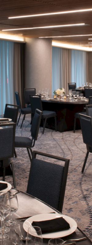 The image shows an elegantly set up event hall with round tables, chairs, and tableware, ready for a formal gathering or banquet.
