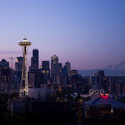 This image shows the Seattle skyline at dusk, featuring the Space Needle and other buildings, with Mount Rainier visible in the background.